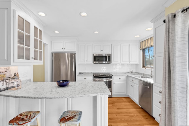 kitchen featuring a sink, appliances with stainless steel finishes, a peninsula, white cabinets, and glass insert cabinets