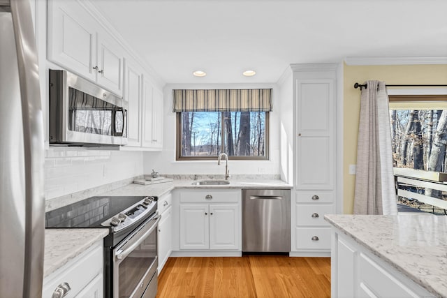 kitchen with a sink, stainless steel appliances, white cabinetry, light wood-type flooring, and backsplash