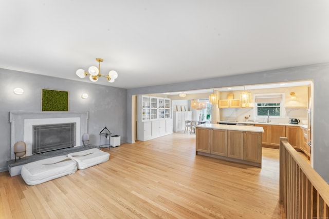 kitchen with a fireplace with raised hearth, light countertops, light wood-style floors, a notable chandelier, and a center island