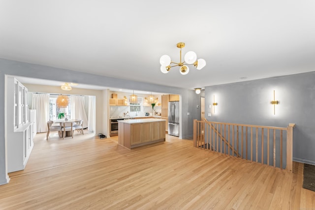 kitchen with light wood-style flooring, a notable chandelier, a kitchen island, and stainless steel appliances