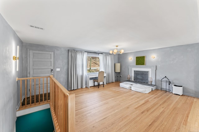 living room featuring a notable chandelier, visible vents, a fireplace with raised hearth, and wood finished floors