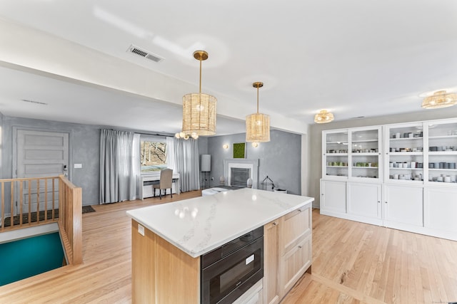 kitchen with visible vents, a kitchen island, black microwave, light wood-style flooring, and hanging light fixtures