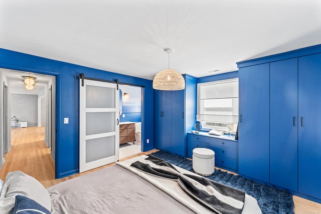 bedroom with light wood finished floors, visible vents, and a barn door