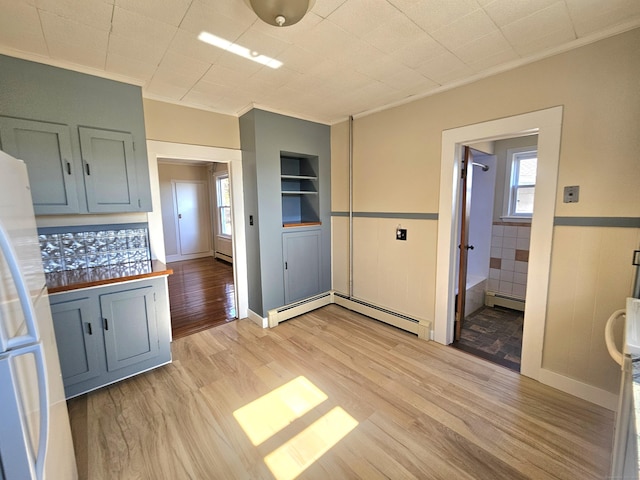 kitchen with baseboard heating, light wood-type flooring, freestanding refrigerator, and ornamental molding