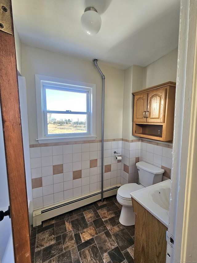 bathroom with a wainscoted wall, toilet, a baseboard heating unit, stone finish flooring, and tile walls