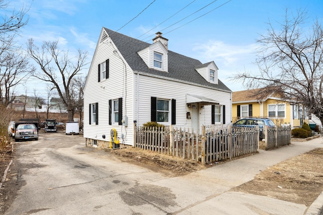 new england style home with a fenced front yard, roof with shingles, and a chimney