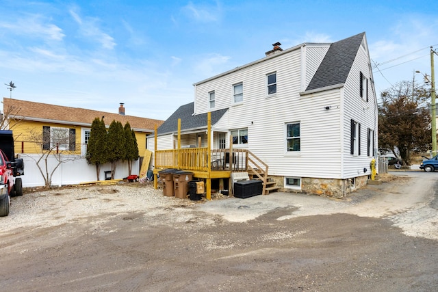 back of house with a wooden deck, roof with shingles, and a chimney