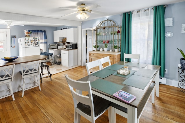 dining area with light wood finished floors, a baseboard heating unit, and a ceiling fan