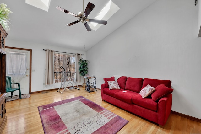 living area featuring high vaulted ceiling, a ceiling fan, wood finished floors, a skylight, and baseboards