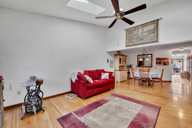 living area with a skylight, baseboards, wood finished floors, and a ceiling fan