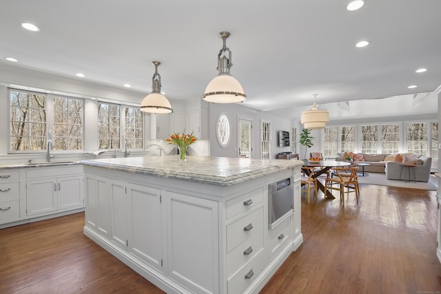 kitchen featuring a sink, light stone counters, dark wood-style floors, a center island, and white cabinetry