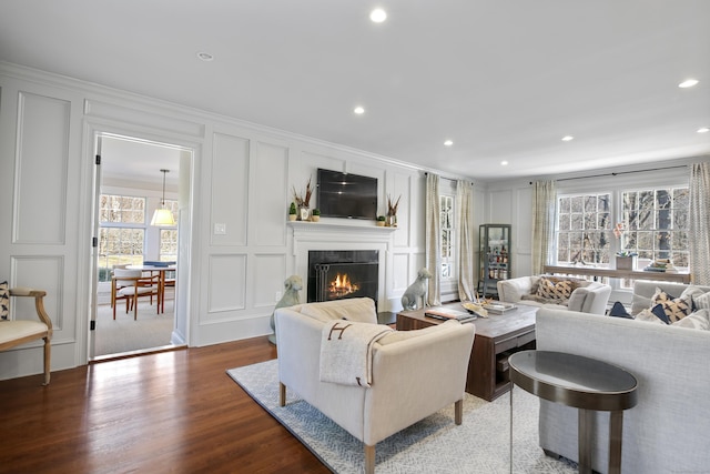 living area featuring a wealth of natural light, wood finished floors, a tiled fireplace, and a decorative wall