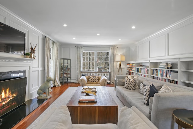 living room featuring built in features, wood finished floors, a lit fireplace, crown molding, and a decorative wall