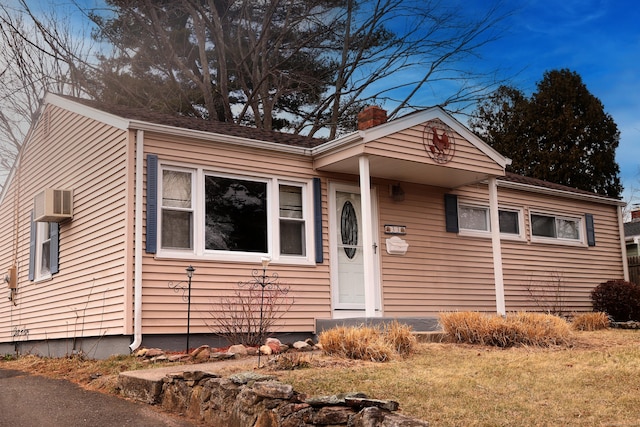 view of front of home with a chimney, a wall mounted AC, and a front yard