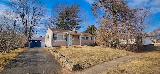 view of front facade with a front yard, an outbuilding, and driveway