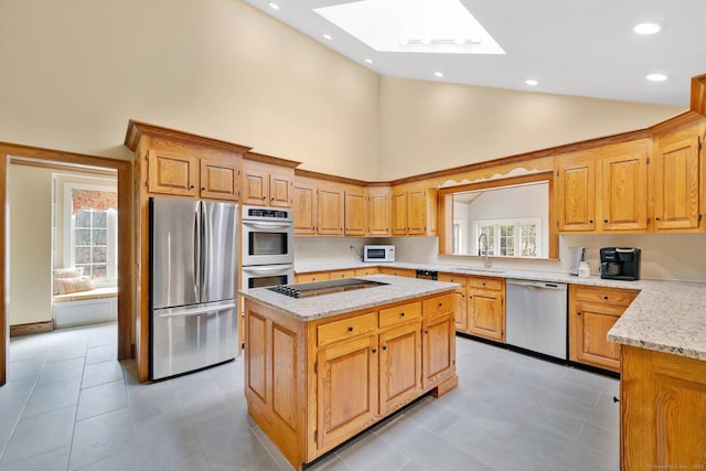 kitchen with light stone countertops, a skylight, a sink, appliances with stainless steel finishes, and a center island