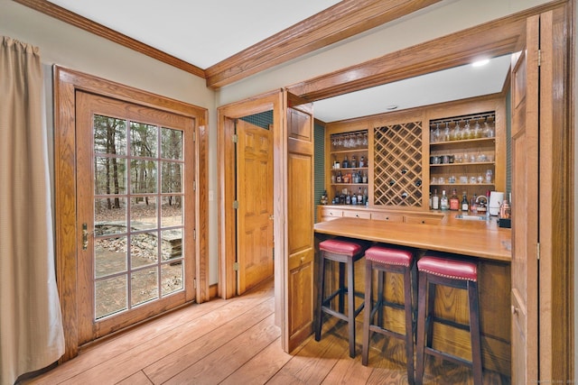 wine cellar with a sink, light wood-style flooring, a dry bar, and ornamental molding