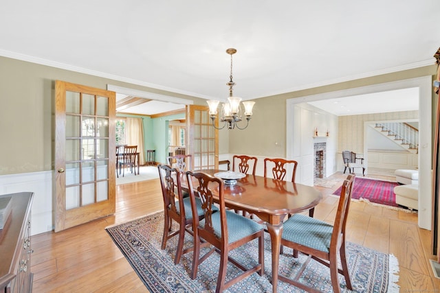 dining room featuring a notable chandelier, ornamental molding, stairs, and light wood finished floors