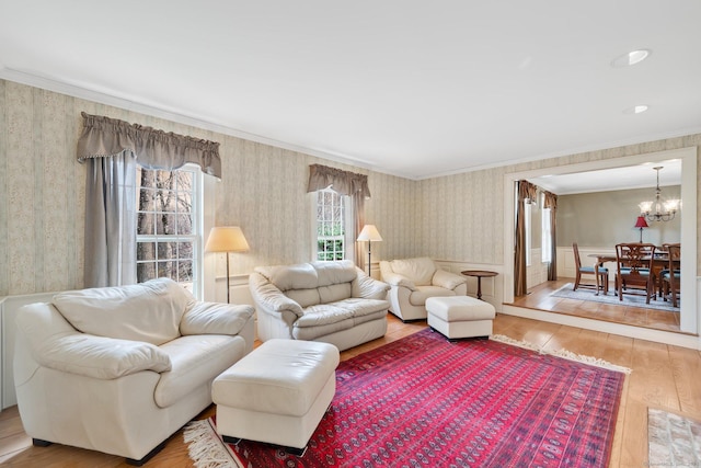 living room with a wainscoted wall, wallpapered walls, hardwood / wood-style flooring, crown molding, and a chandelier