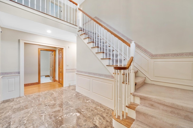 stairway featuring wainscoting, a decorative wall, marble finish floor, and a towering ceiling