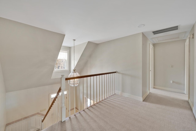 hallway with visible vents, an upstairs landing, baseboards, and carpet flooring