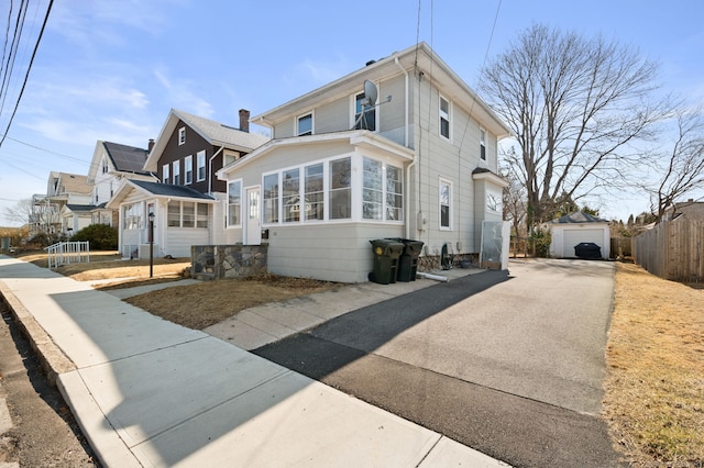 view of front of home with an outdoor structure, fence, a detached garage, and aphalt driveway