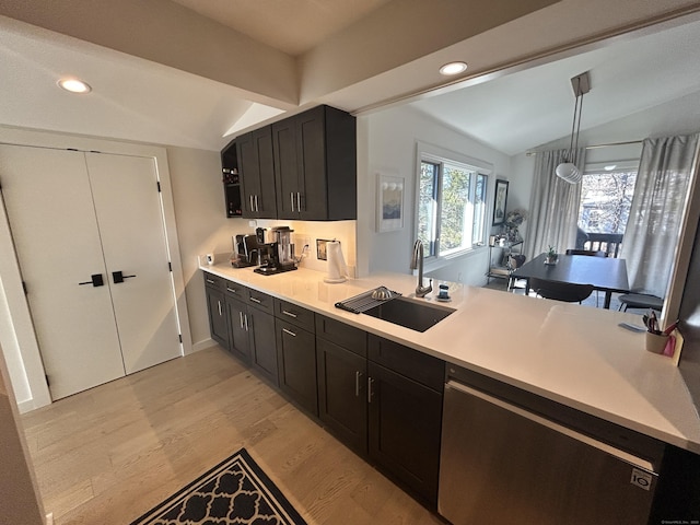 kitchen with a sink, light countertops, lofted ceiling, light wood-style flooring, and stainless steel dishwasher