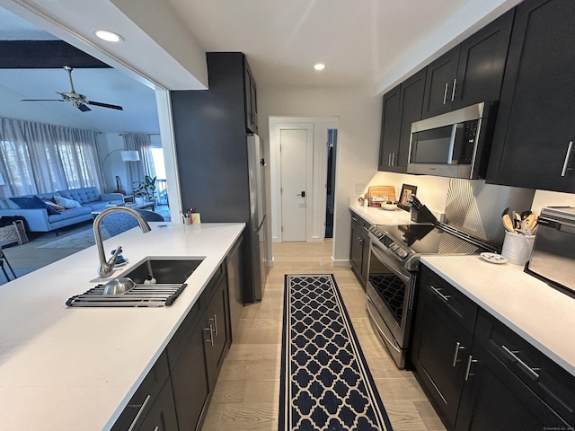 kitchen with appliances with stainless steel finishes, light countertops, dark cabinetry, and a sink