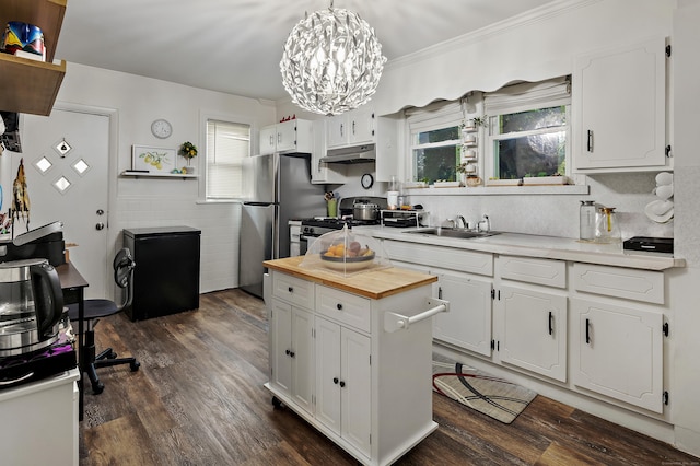 kitchen with a sink, white cabinets, under cabinet range hood, appliances with stainless steel finishes, and butcher block counters