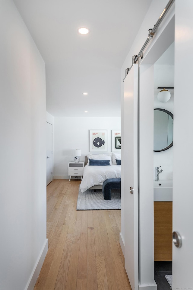 hallway with baseboards, a barn door, light wood-style flooring, and recessed lighting