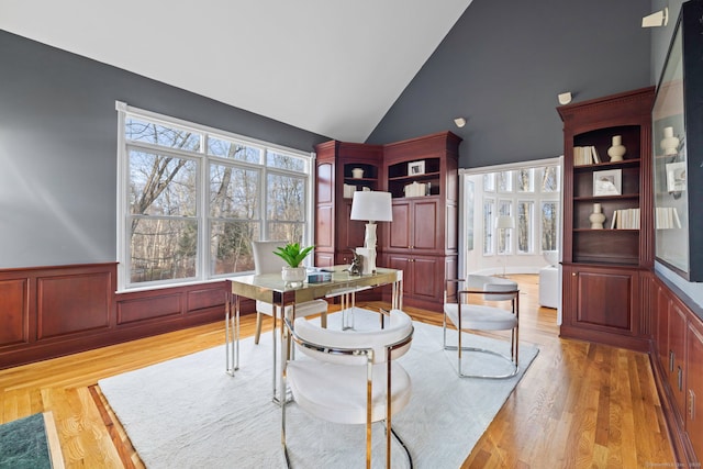 office with high vaulted ceiling, light wood-style floors, and wainscoting