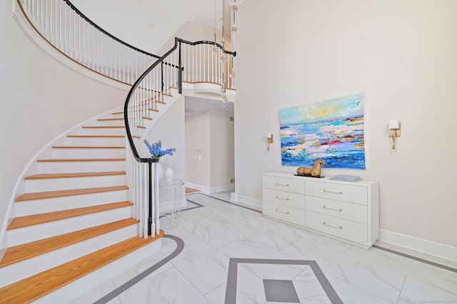 stairway with marble finish floor, baseboards, and a towering ceiling