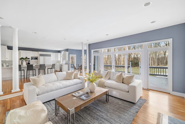 living area featuring recessed lighting, baseboards, light wood-style flooring, and ornate columns