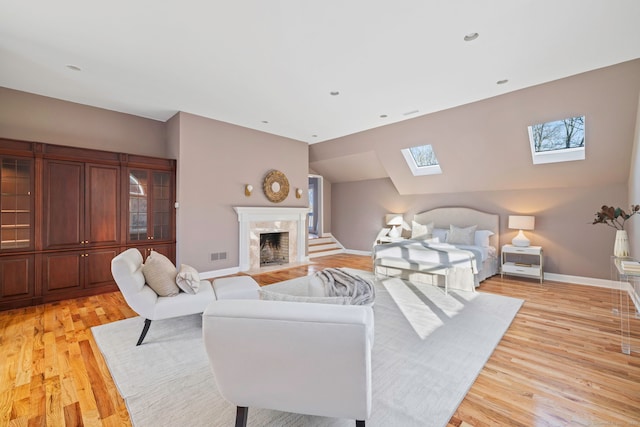 bedroom featuring light wood-type flooring, visible vents, a high end fireplace, vaulted ceiling with skylight, and baseboards