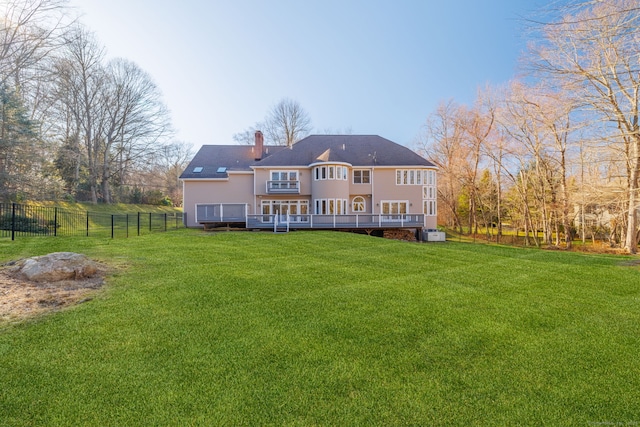 rear view of property with fence, a shingled roof, a chimney, a deck, and a lawn