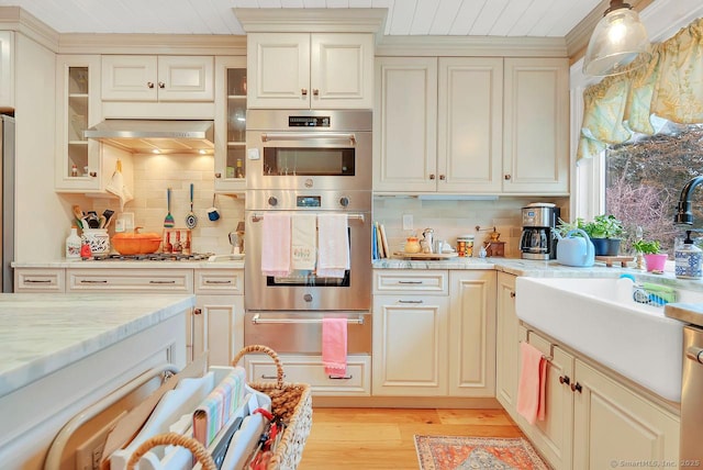 kitchen featuring under cabinet range hood, appliances with stainless steel finishes, cream cabinets, and a warming drawer