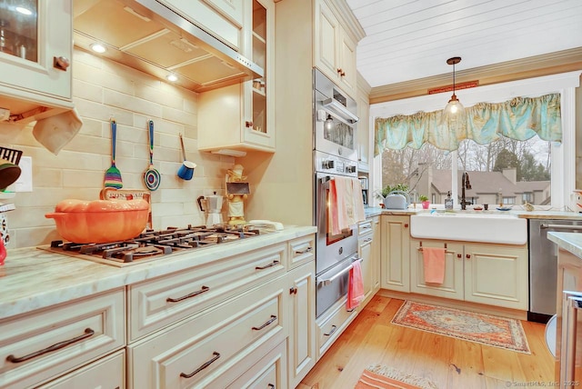 kitchen featuring light wood-type flooring, under cabinet range hood, a sink, stainless steel appliances, and decorative backsplash