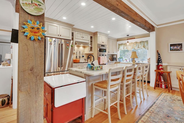 kitchen with an island with sink, appliances with stainless steel finishes, crown molding, cream cabinets, and light wood-type flooring