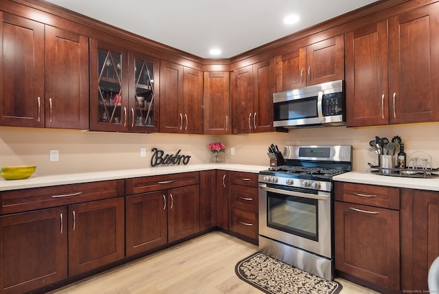 kitchen with light countertops, light wood-style flooring, glass insert cabinets, and appliances with stainless steel finishes