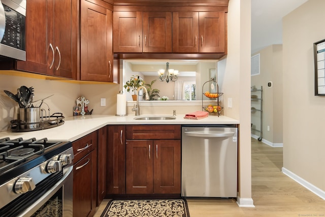 kitchen with a sink, appliances with stainless steel finishes, light wood finished floors, baseboards, and light countertops