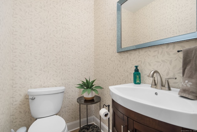 half bath with toilet, wallpapered walls, baseboards, and a sink