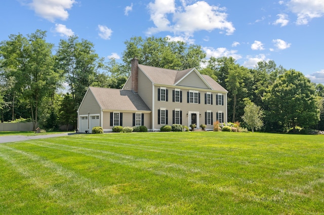 colonial-style house with a front yard, an attached garage, fence, and a chimney