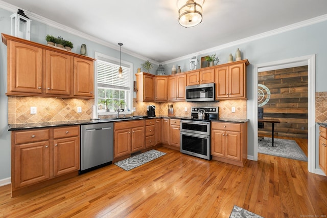 kitchen with light wood finished floors, pendant lighting, ornamental molding, appliances with stainless steel finishes, and a sink