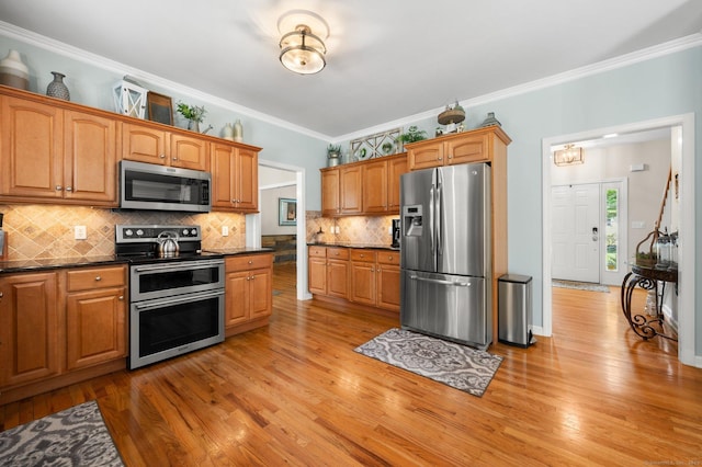 kitchen featuring light wood-style flooring, backsplash, dark countertops, appliances with stainless steel finishes, and crown molding