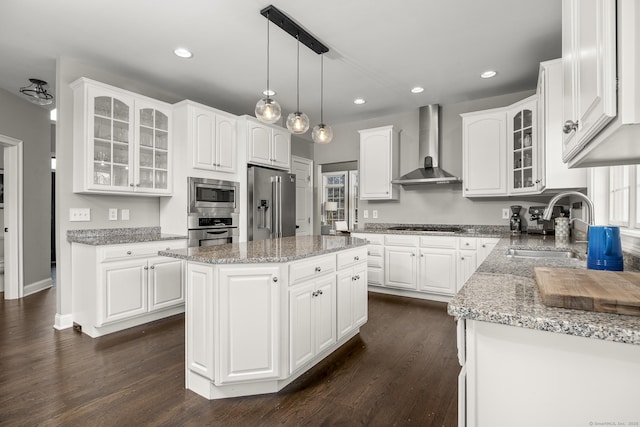 kitchen with a sink, dark wood-style floors, appliances with stainless steel finishes, white cabinets, and wall chimney range hood