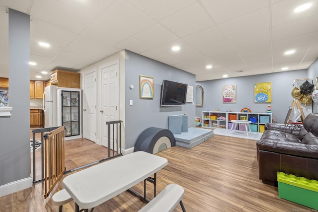 living room with a drop ceiling, recessed lighting, light wood-type flooring, and baseboards