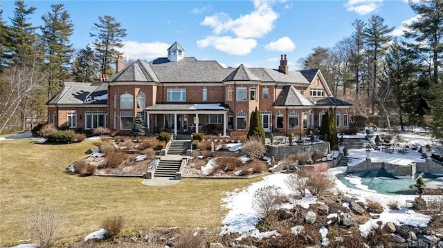 back of house featuring brick siding, a chimney, stairs, and a yard