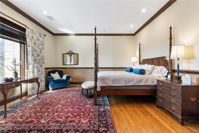 bedroom with light wood finished floors, visible vents, wainscoting, and crown molding