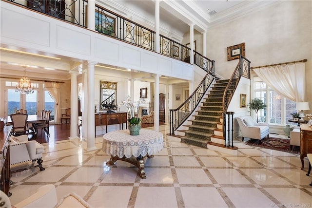 entrance foyer with a chandelier, ornamental molding, stairs, and decorative columns