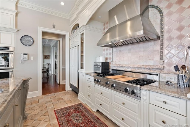 kitchen with tasteful backsplash, crown molding, wall chimney range hood, white cabinets, and stainless steel appliances